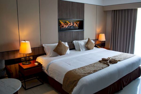 A neatly arranged hotel room with a large bed, bedside lamps, decorative pillows, and a wall art piece above the headboard.