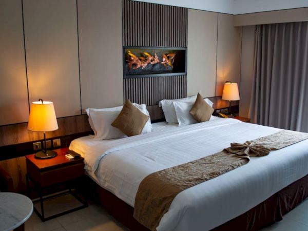 A neatly arranged hotel room with a large bed, bedside lamps, decorative pillows, and a wall art piece above the headboard.