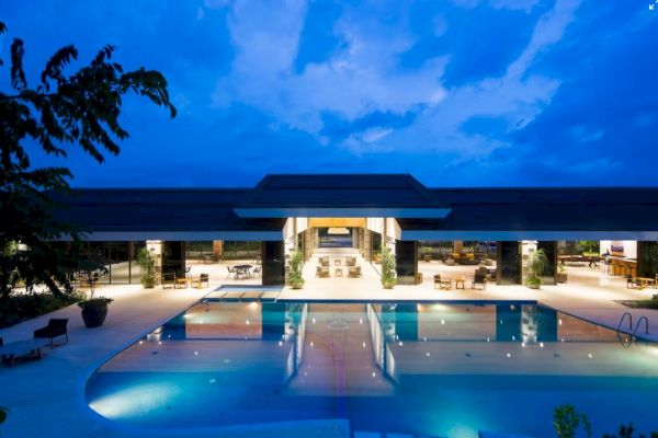 A luxurious building with an illuminated pool at dusk, under a vibrant blue sky.