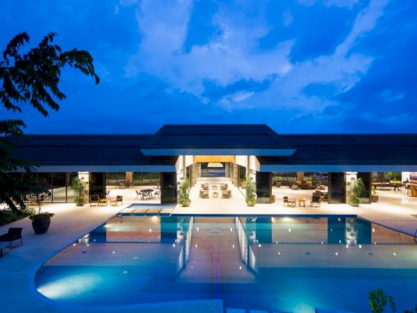 A luxurious building with an illuminated pool at dusk, under a vibrant blue sky.
