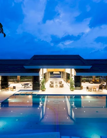 A luxurious swimming pool at night with surrounding modern architecture and dim lighting, under a partly cloudy sky.