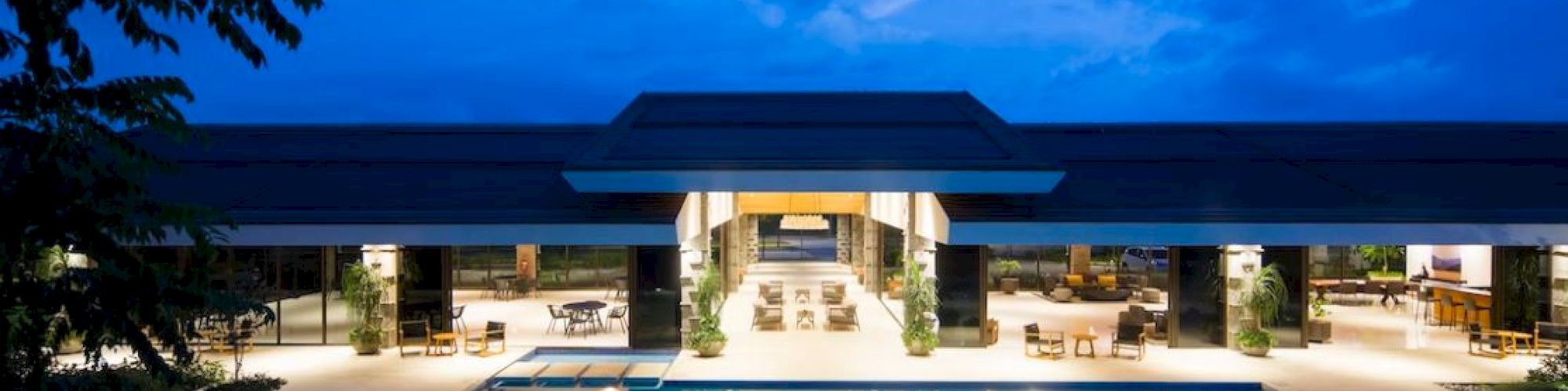 A luxurious building with open-air lounges and a large pool, under a dramatic evening sky.