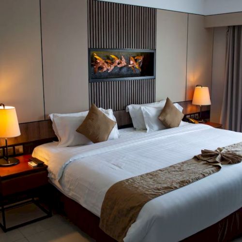A cozy hotel room with a large bed, decorative pillows, bedside lamps, and elegant wall art; curtains open slightly to the right.