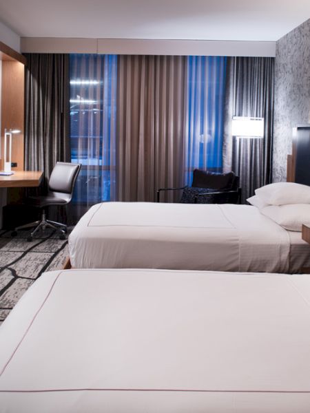 A modern hotel room with two beds, a TV, desk, chair, and a patterned accent wall.