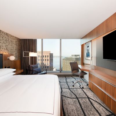 A modern hotel room with a large bed, wall-mounted TV, desk, and a city view through large windows completes the stylish look.