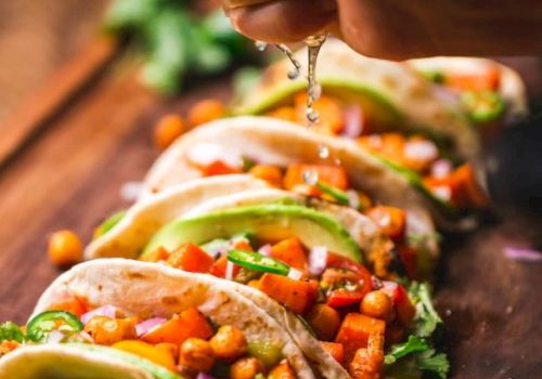 A person is squeezing lime over tacos filled with chickpeas, avocado, and vegetables arranged on a wooden board.