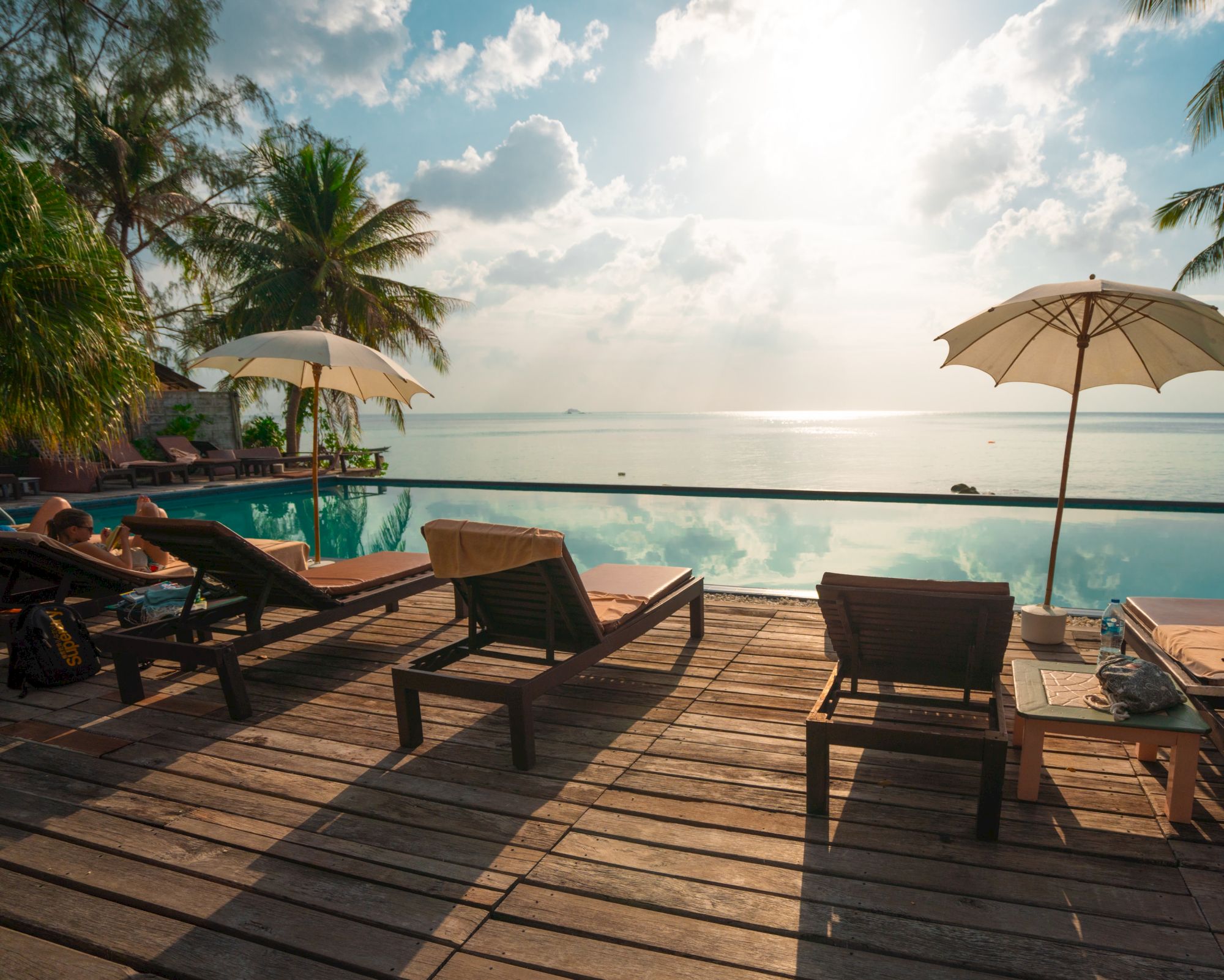 A serene poolside scene with lounge chairs, umbrellas, and tropical views over a calm sea at sunrise or sunset.