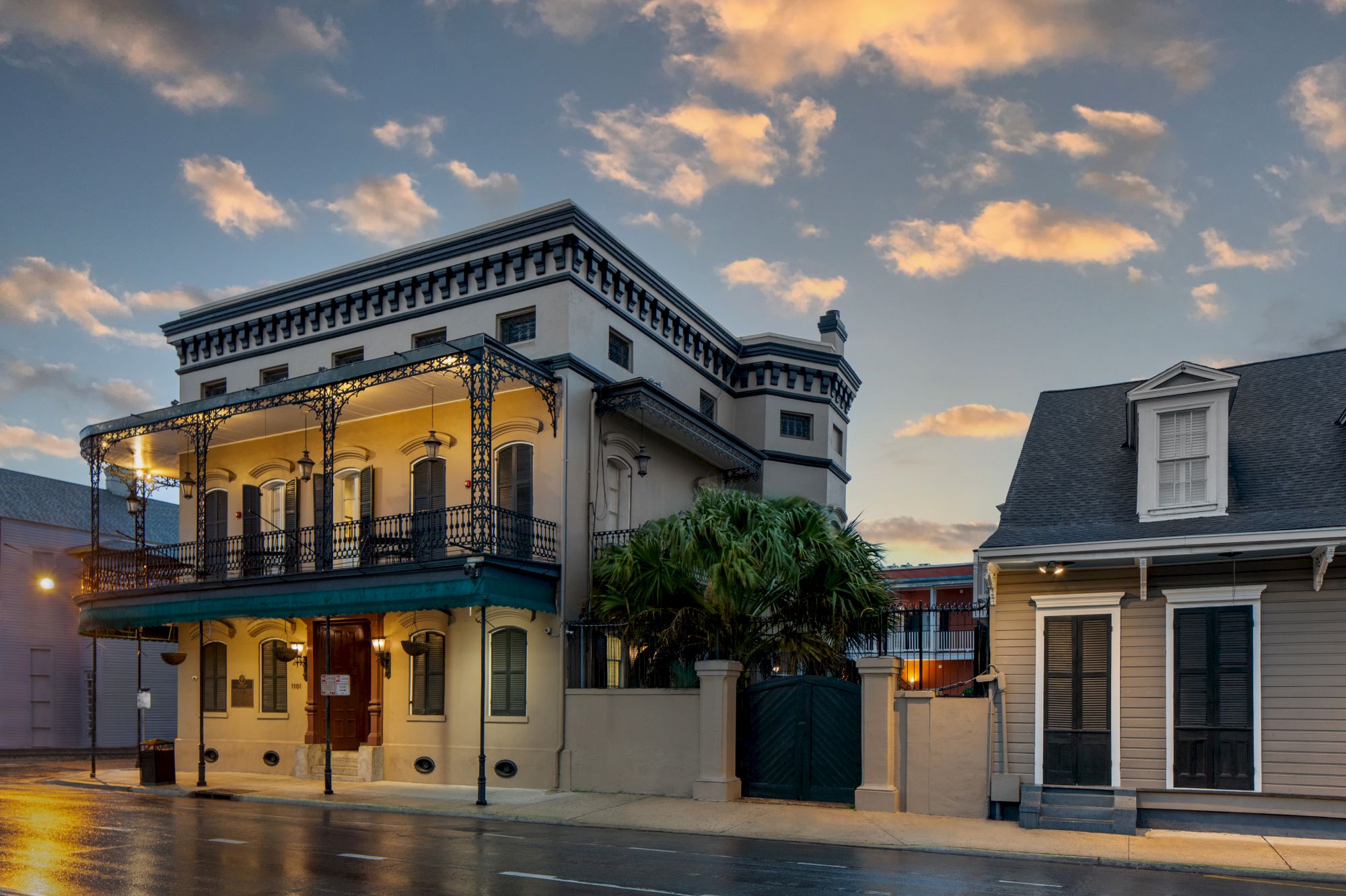 The image shows a historic building with balconies and ornate ironwork beside a more modern house, set against a cloudy evening sky.