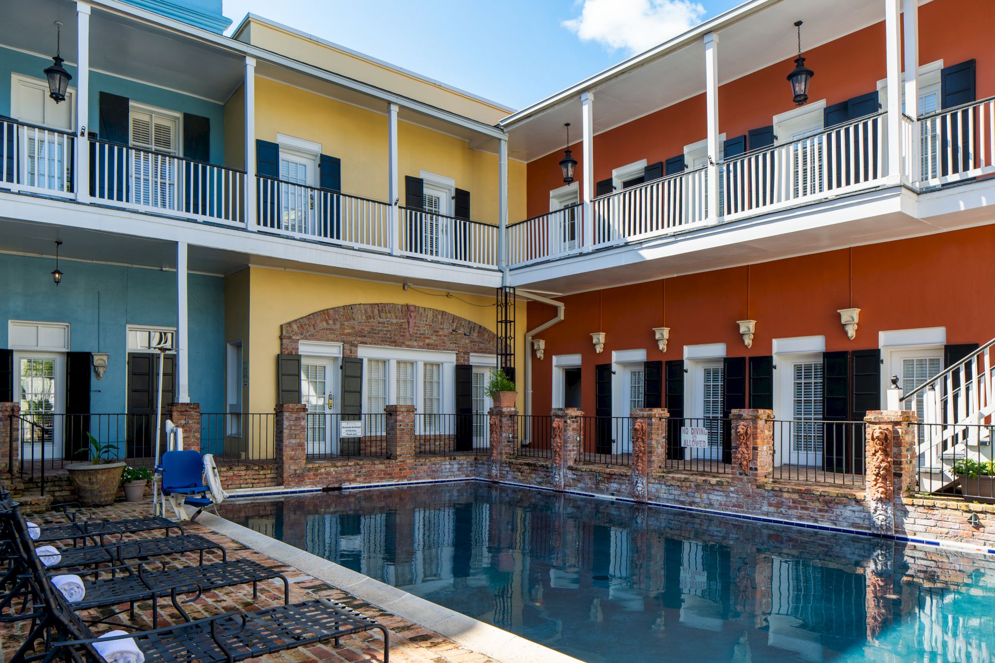A courtyard with a swimming pool, surrounded by colorful two-story buildings with balconies and deck chairs by the water's edge.