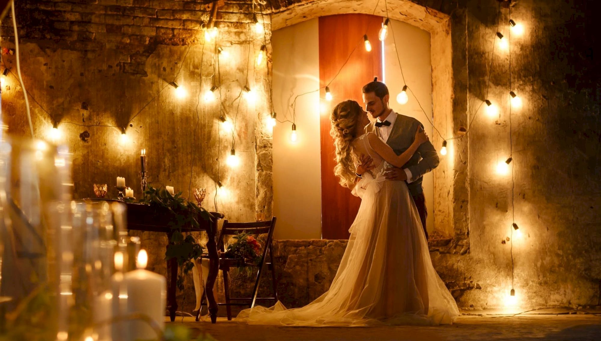 A couple dances in a warmly lit room with candles and string lights, creating a romantic ambiance.