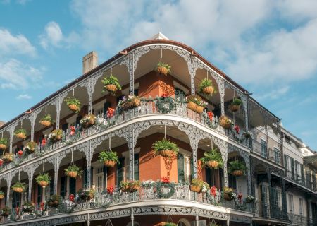 A historic building with intricate ironwork balconies and potted plants under a blue sky with clouds.