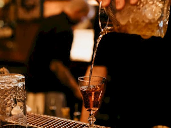 A bartender is pouring a drink into a glass with a straw, behind a bar counter.
