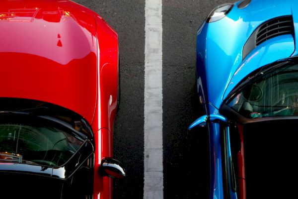 Aerial view of a red car and a blue car parked next to each other, separated by a white line on asphalt.