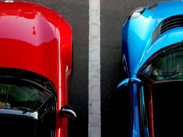 Aerial view of a red car and a blue car parked next to each other, separated by a white line on asphalt.