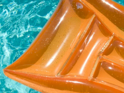 An orange inflatable raft floats on clear blue water, sunlight glinting off its glossy surface, ready for a seaside ride.