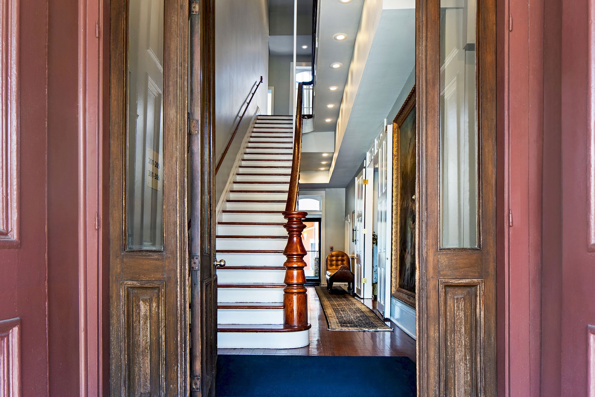 A classic wooden staircase at a bright hallway, with carpet runners, paneled walls, and a wooden banister appearing inside a warm, inviting home.
