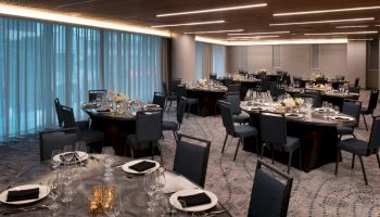 The image shows a banquet room set up with round tables, chairs, elegant table settings, and subtle lighting, ready for an event.