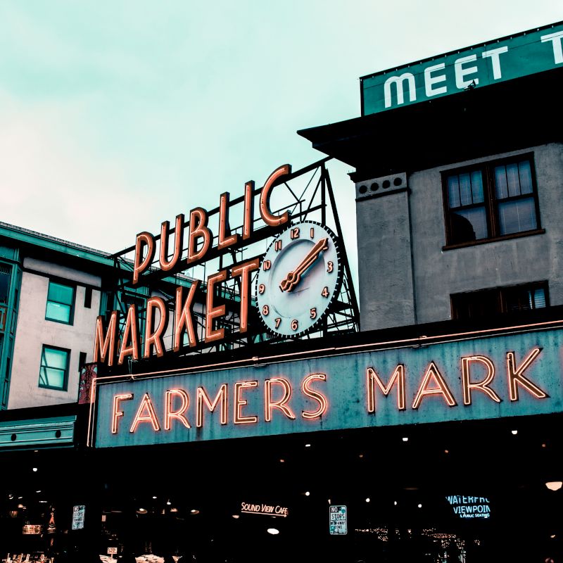 The image shows the iconic neon sign for the "Public Market" and "Farmers Market," with a clock, likely at a popular market location.