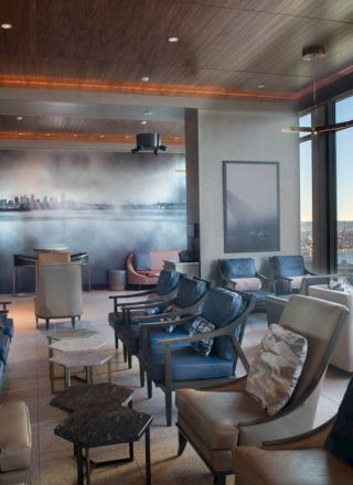 A modern lounge with plush seating, large windows offering a scenic view, and stylish decor featuring a cityscape wall mural.