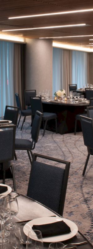 The image shows a banquet hall with round tables set for dining, featuring black tablecloths, elegant place settings, and dim lighting.