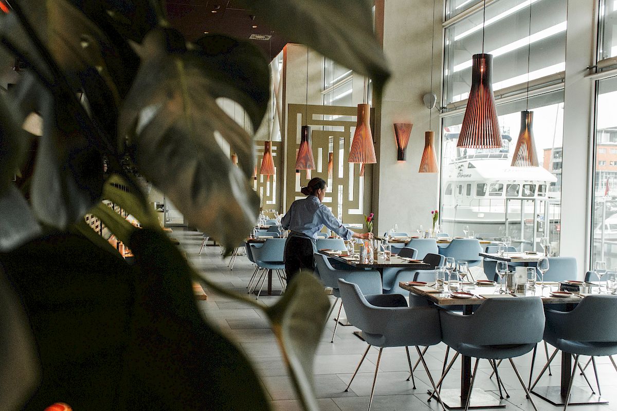 A person is arranging tables in a modern restaurant with stylish lighting and large windows.